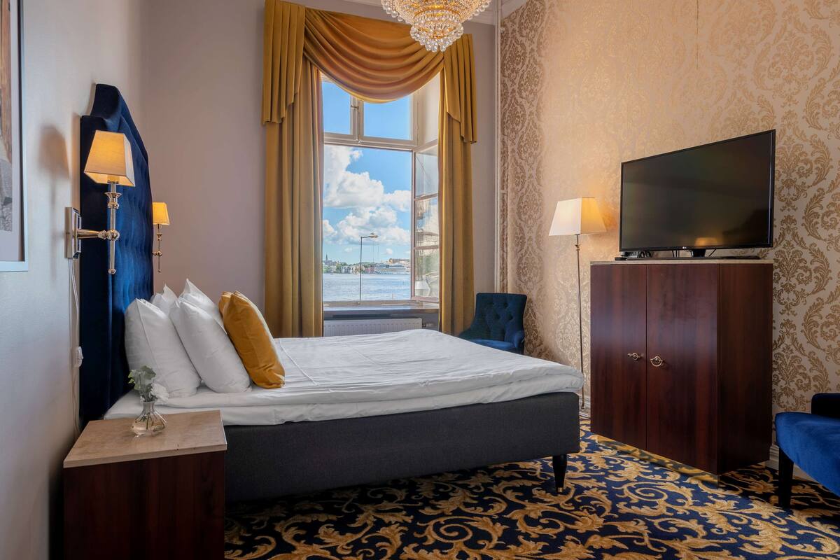 A hotel room with a bed, a television, a wardrobe, and a view of the outdoors.