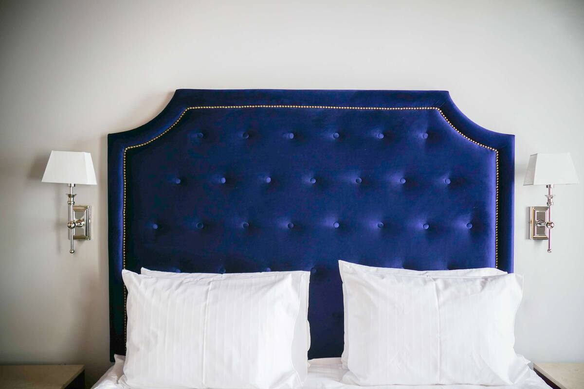 A hotel room with a tufted headboard, two white pillows, and bedside lamps.
