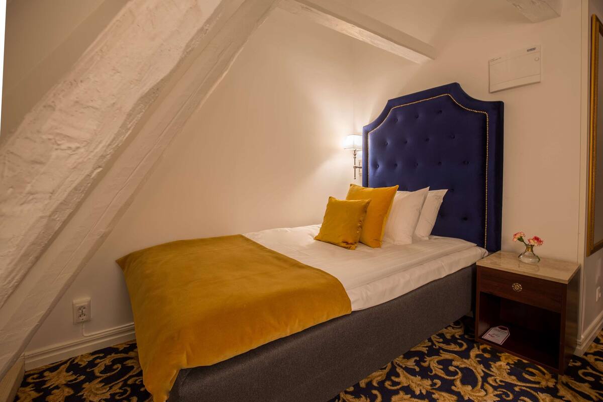A bedroom with a blue headboard, a yellow throw blanket, and a patterned carpet.