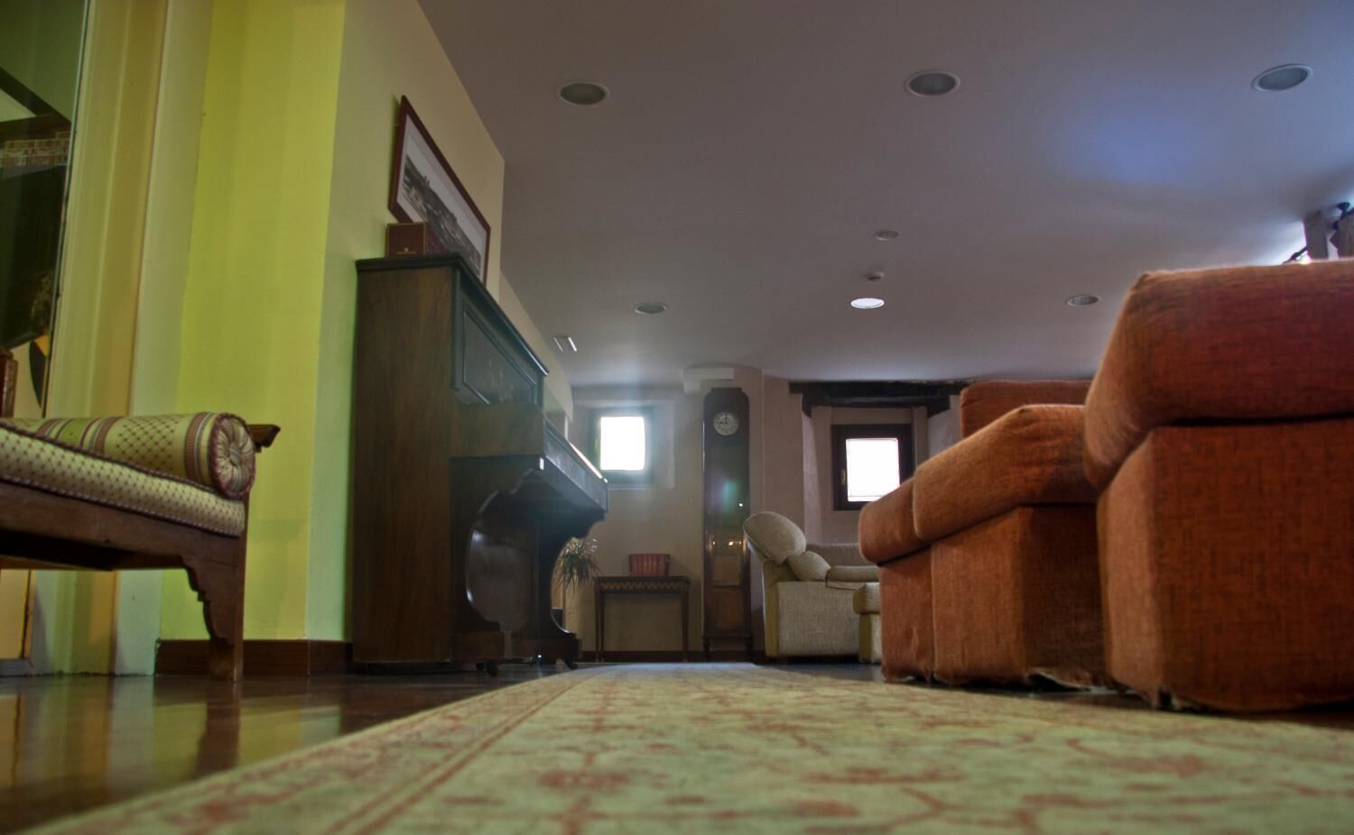 A living room with a sofa, armchair, and a piano.