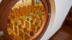 A circular window overlooking a room with rows of wooden chairs and tables, suggesting a conference or meeting space. - Hospedería Porta Coeli (Siguenza)