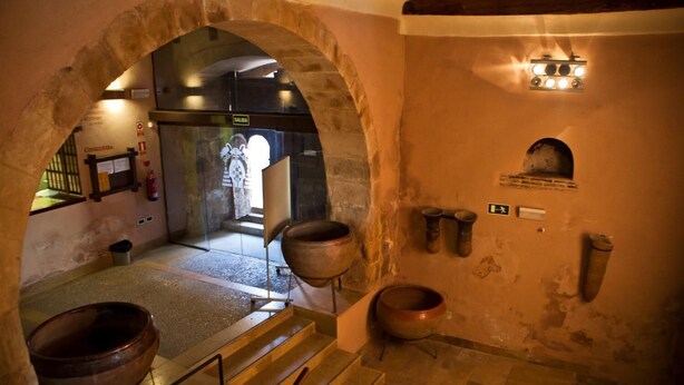 A historical building with arched doorways, a large copper pot, and a staircase leading to an upper level. - Hospedería Porta Coeli (Siguenza)