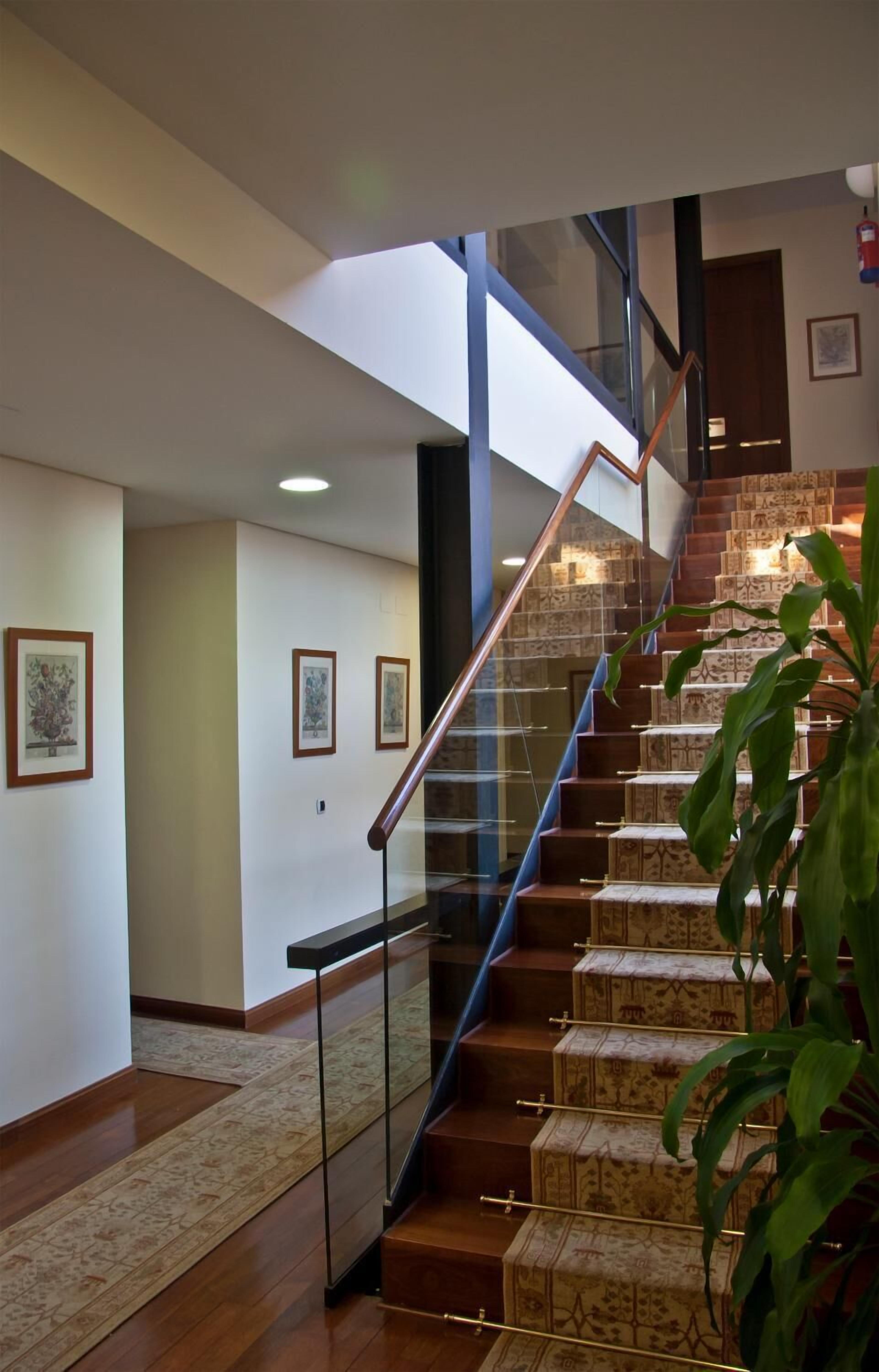 Una escalera moderna con barandas de vidrio y alfombra estampada que sube a un segundo piso.