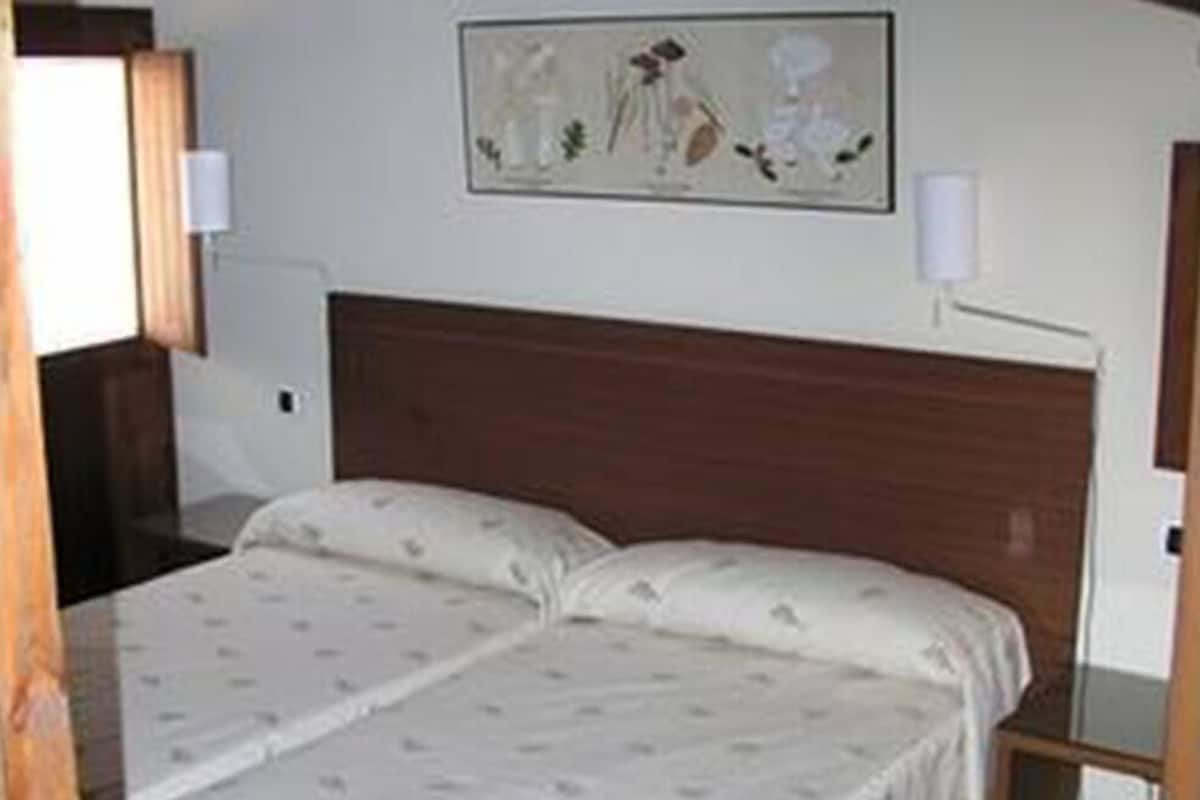 Un dormitorio con una cama doble, cabecera de madera, mesita de noche y lámpara de pared.