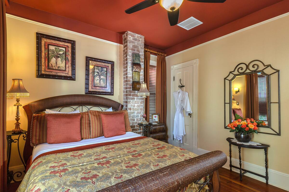 A bedroom with a large bed, a nightstand, a dresser, a mirror, and a window with curtains.