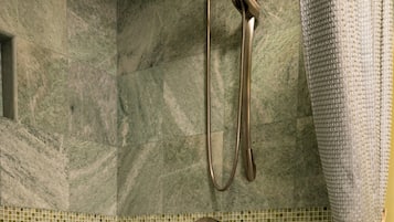 A bathroom with a marble wall, a bathtub with rose petals, a towel, and a shower head.