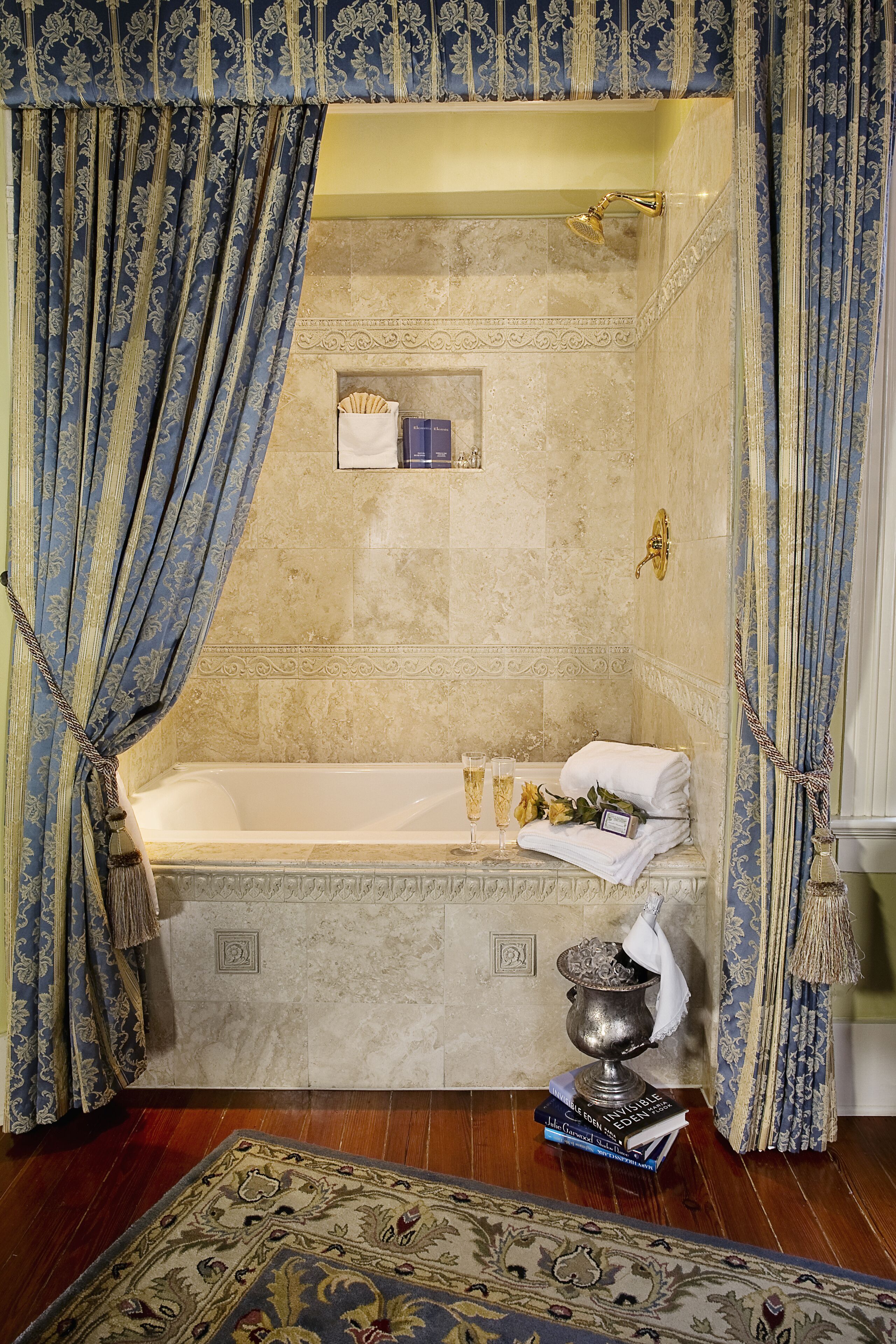 A luxurious bathroom with a marble bathtub, ornate curtains, a decorative rug, and a small shelf with toiletries.