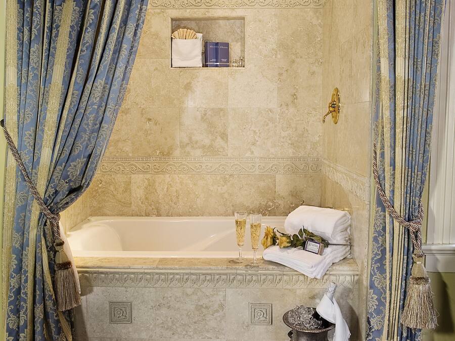 A luxurious bathroom with a marble bathtub, ornate curtains, a decorative rug, and a small shelf with toiletries.