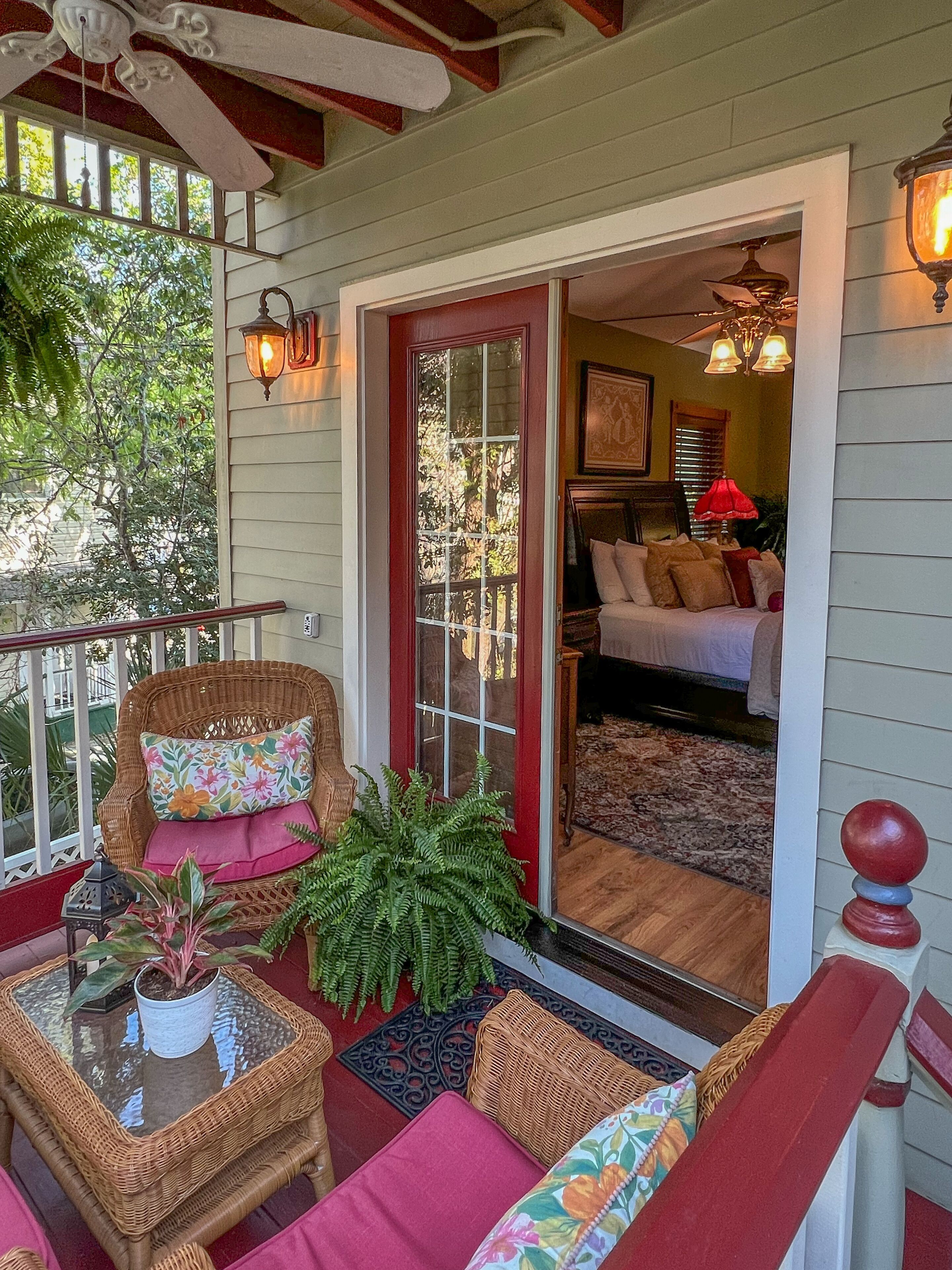 A cozy porch with wicker furniture, a glass table, and a red door leading to a bedroom.