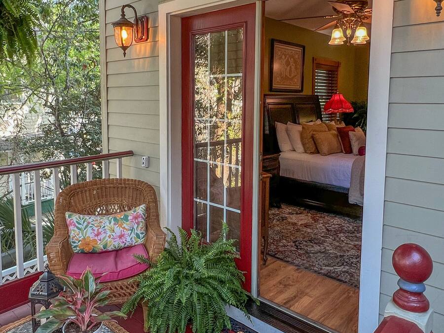 A cozy porch with wicker furniture, a glass table, and a red door leading to a bedroom.