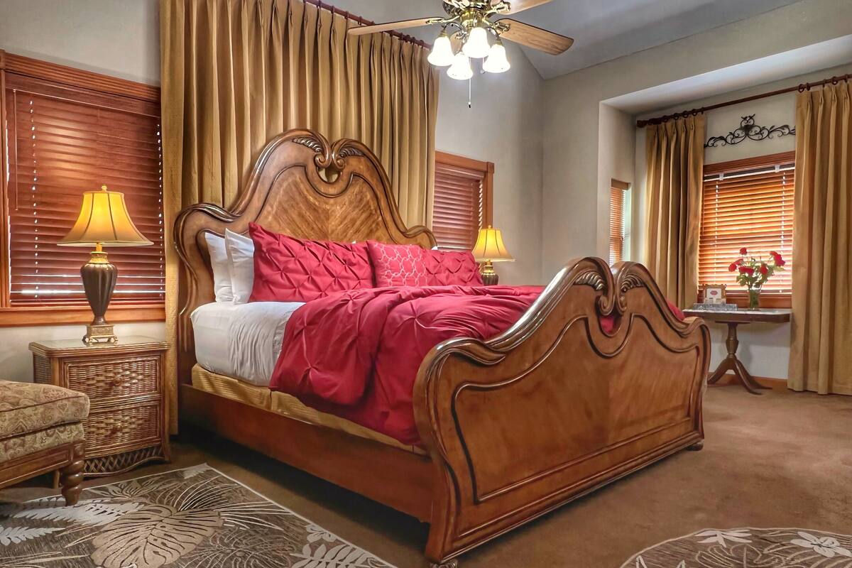A bedroom with a wooden bed, two bedside lamps, a nightstand, a chair, a small table with a vase, and a ceiling fan.