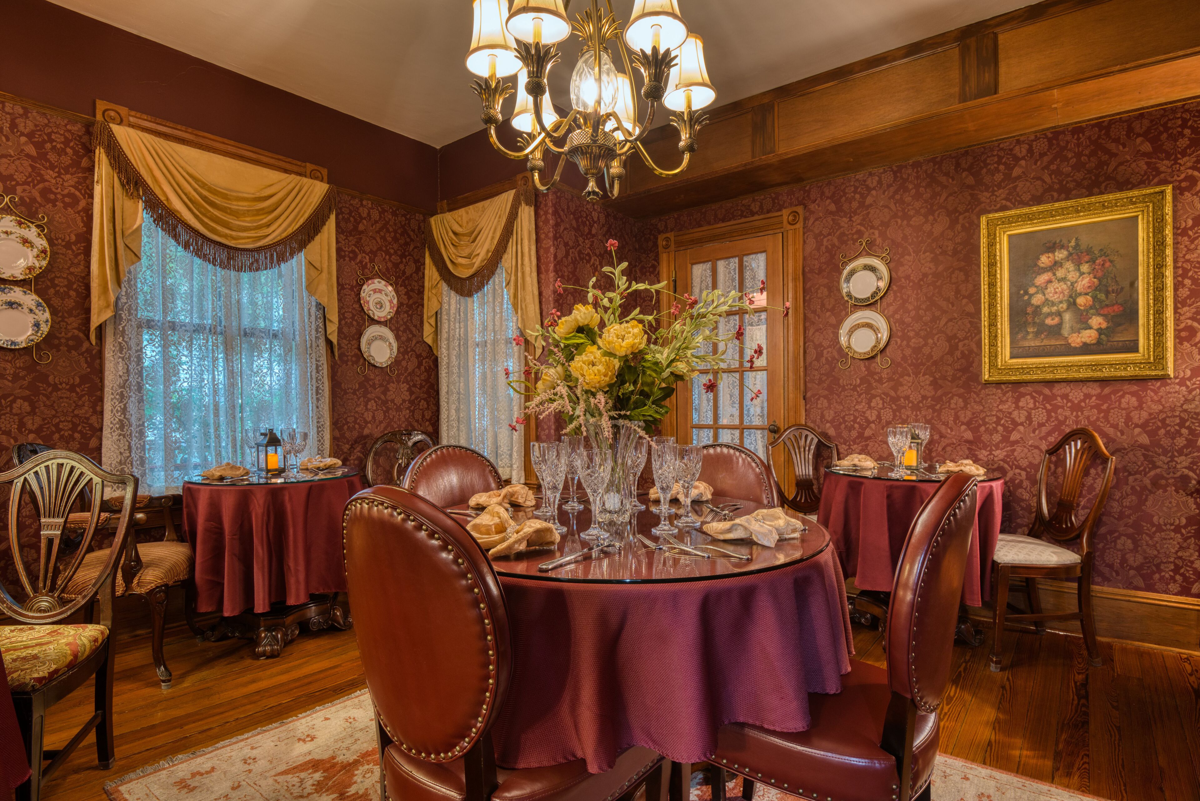 A dining room with a chandelier, floral arrangements, and antique furniture.