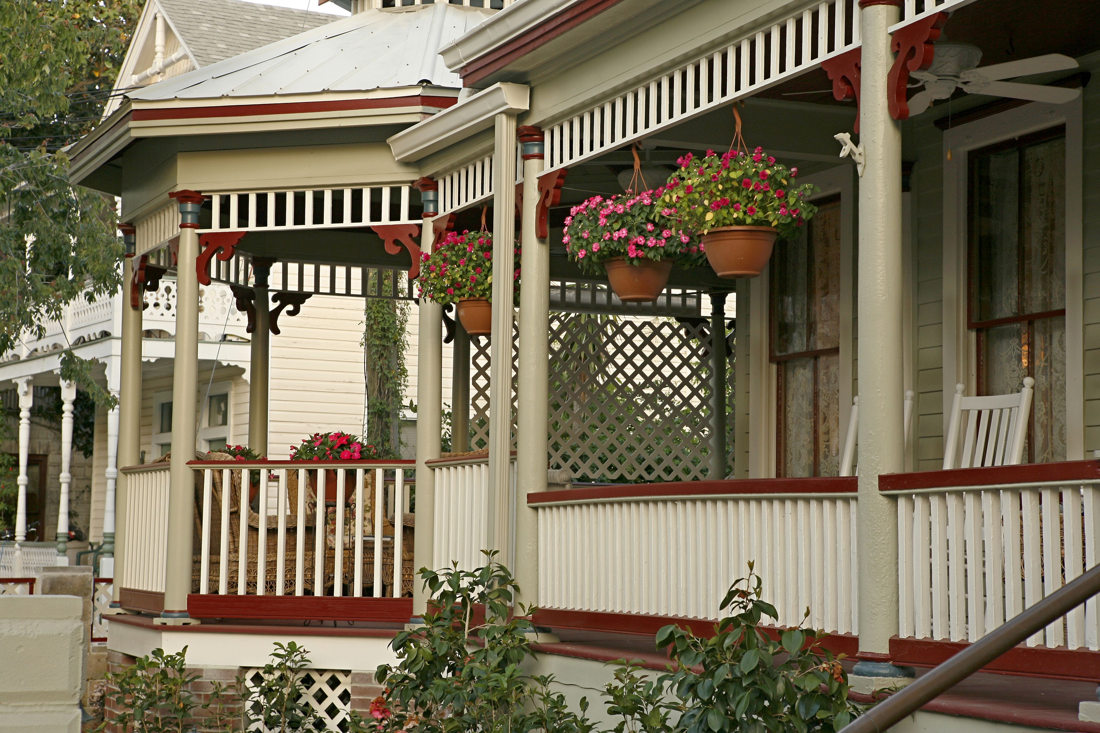 A porch with white railings and red accents, potted plants, and a white chair.
