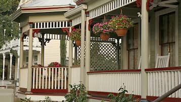 A porch with white railings and red accents, potted plants, and a white chair.