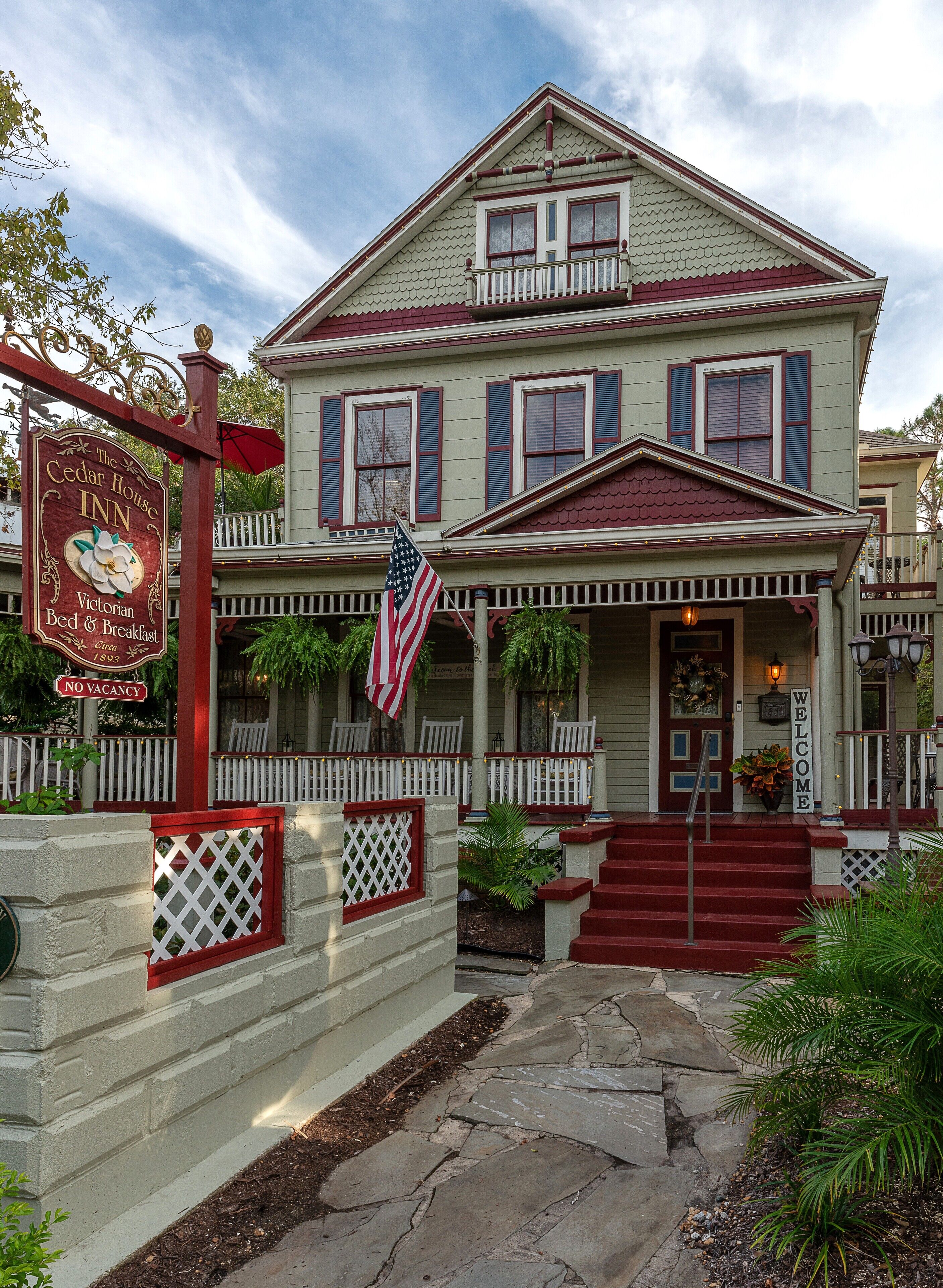 A Victorian-style inn with a red and white facade, a welcoming front porch, and an American flag.
