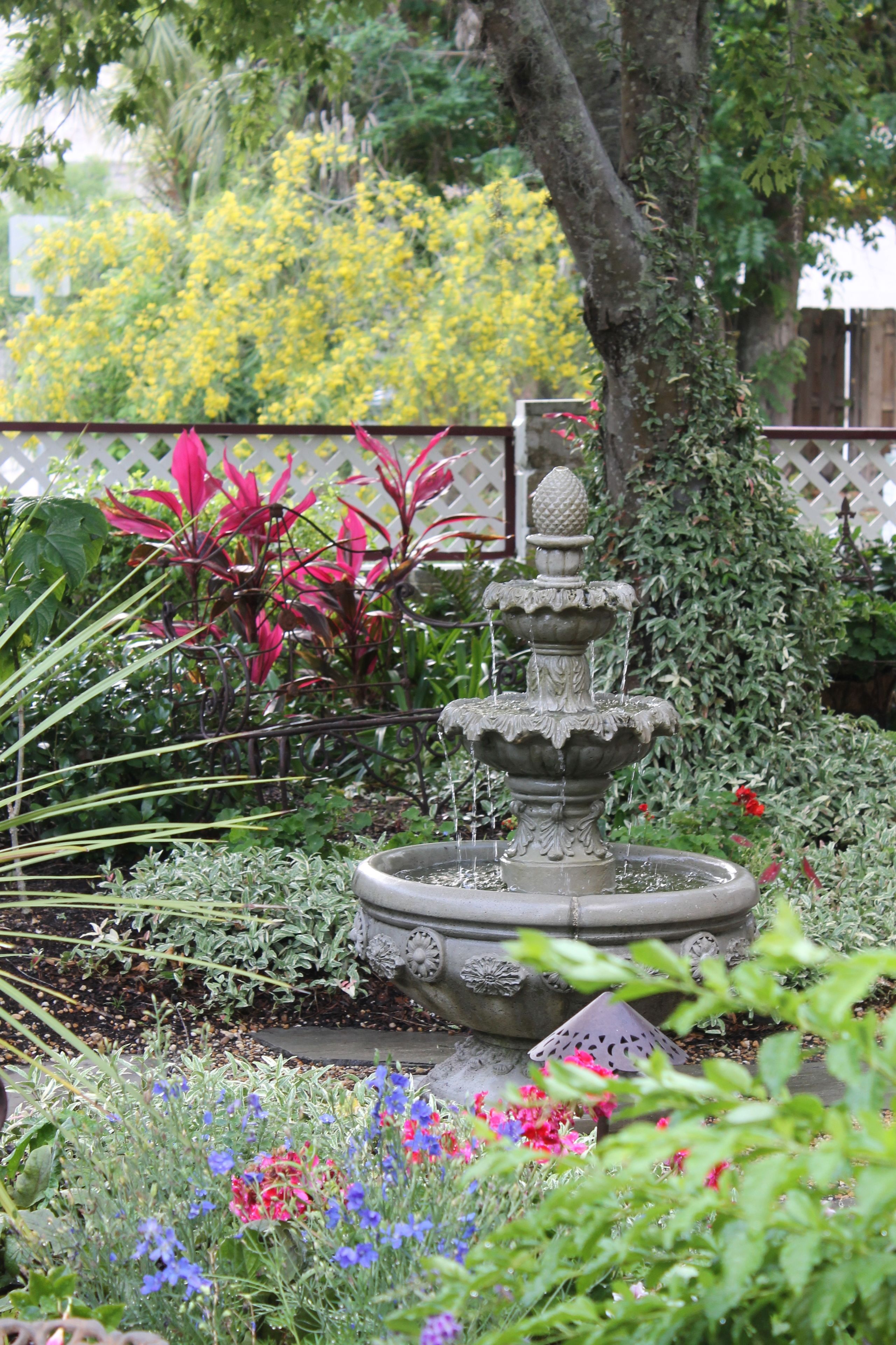 A garden with a multi-tiered fountain, surrounded by various plants and flowers.