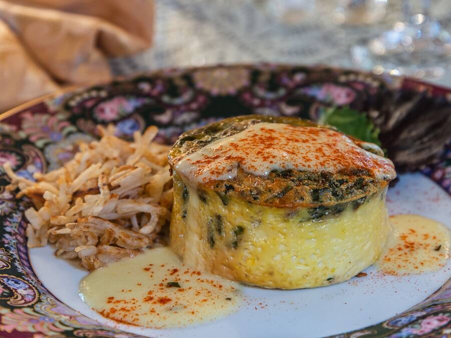 Un plato de comida con un guiso cremoso, posiblemente una quiche, acompañado de carne desmenuzada y una salsa aparte.