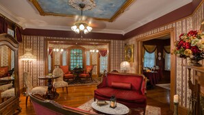 A room with a red sofa, a round table, and a chandelier. There is a mirror, a chair, and a lamp. The room has patterned wallpaper and a wooden floor. - Cedar House Inn (St. Augustine)