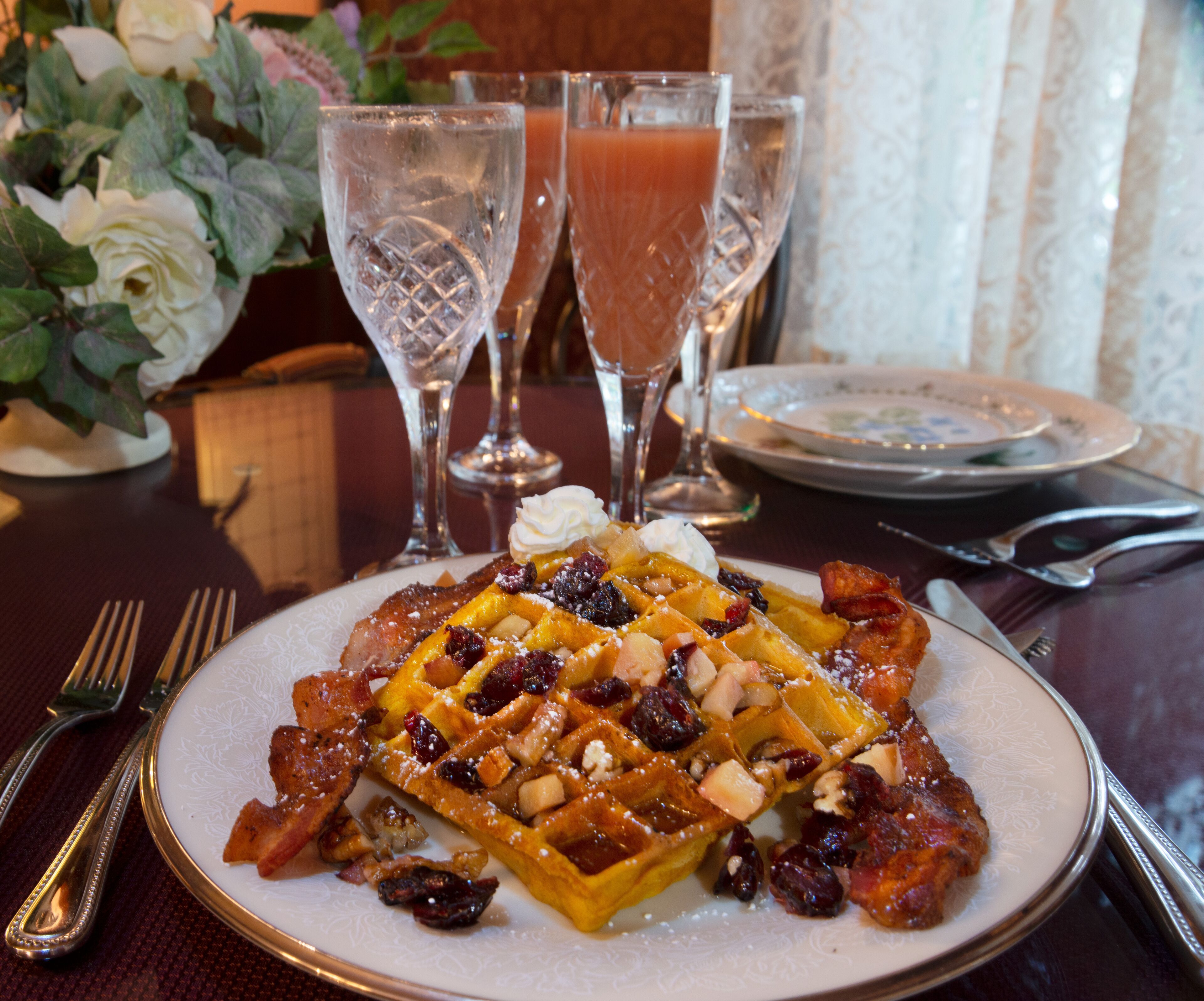 Un plato de gofres con fruta y nueces, acompañado de un vaso de jugo de naranja y un vaso de vino tinto.