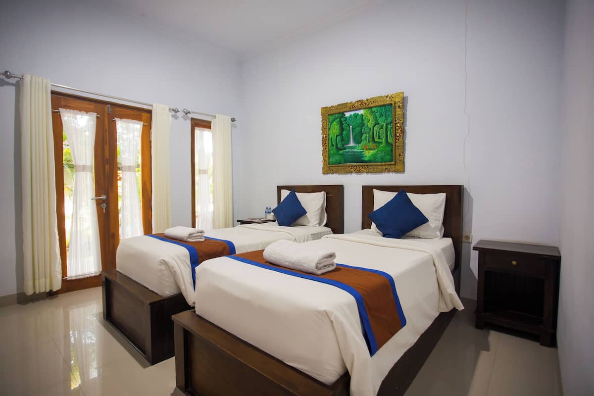 A hotel room with two beds, a painting on the wall, and a wooden nightstand.