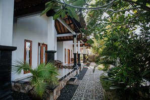 A covered outdoor area with a stone pathway, wooden benches, and potted plants. - The Dagan Bungalow (Penida Island)