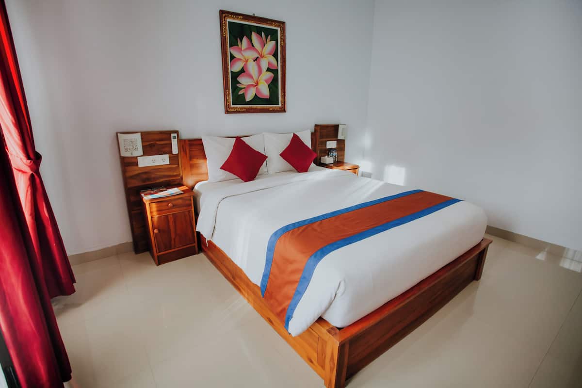 A neatly made bed with a wooden frame, white bedding, and a blue and orange accent. There are two nightstands with lamps and a wall-mounted painting above the bed.