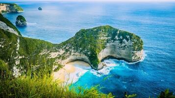 Un paisaje costero con una formación rocosa destacada, aguas azules cristalinas y una playa de arena.