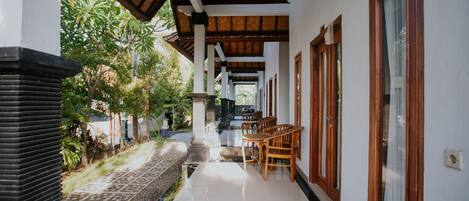 A covered corridor with a tiled floor, wooden furniture, and a view of greenery outside.