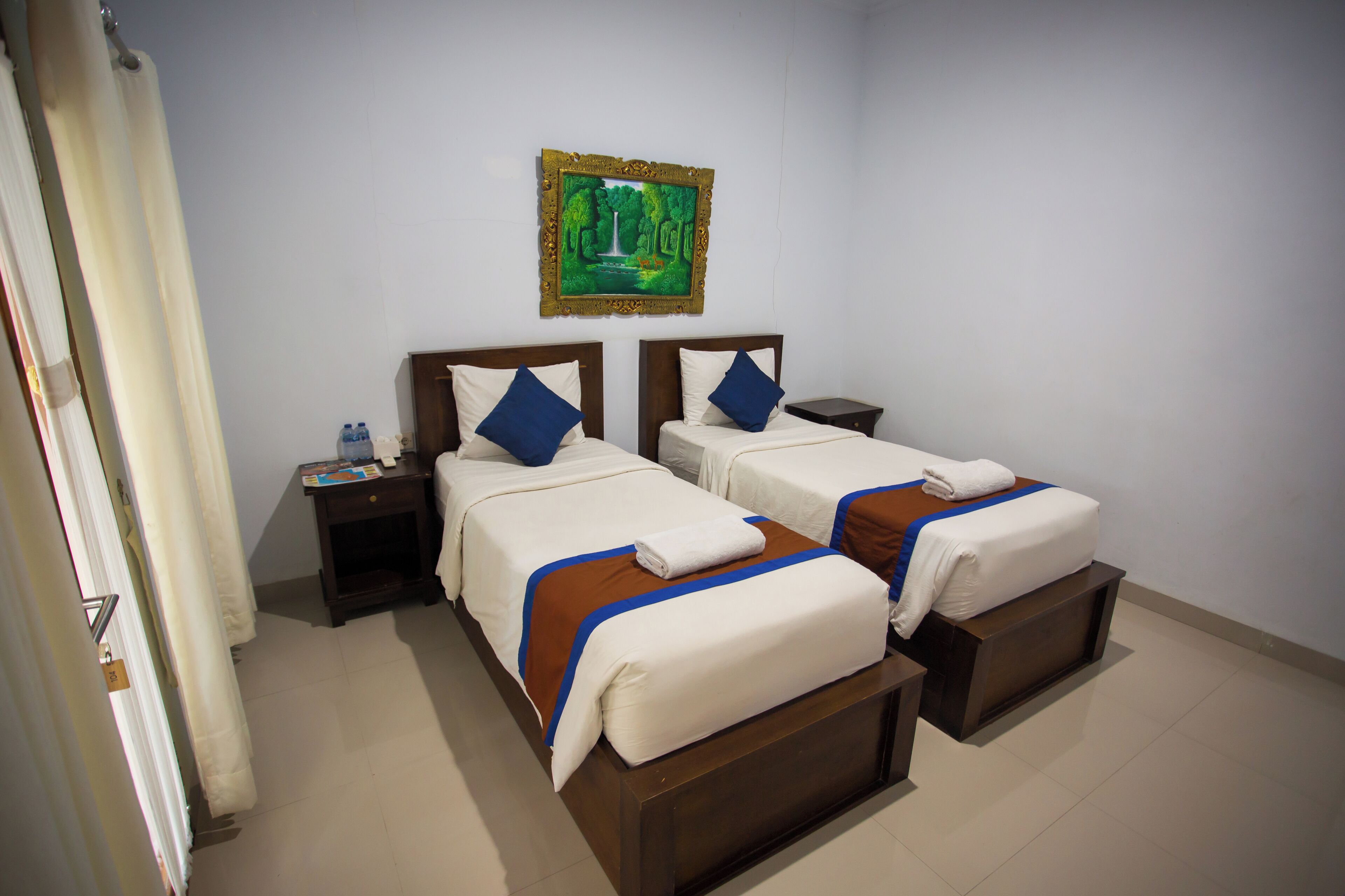 A hotel room with two beds, a nightstand, and a painting on the wall.