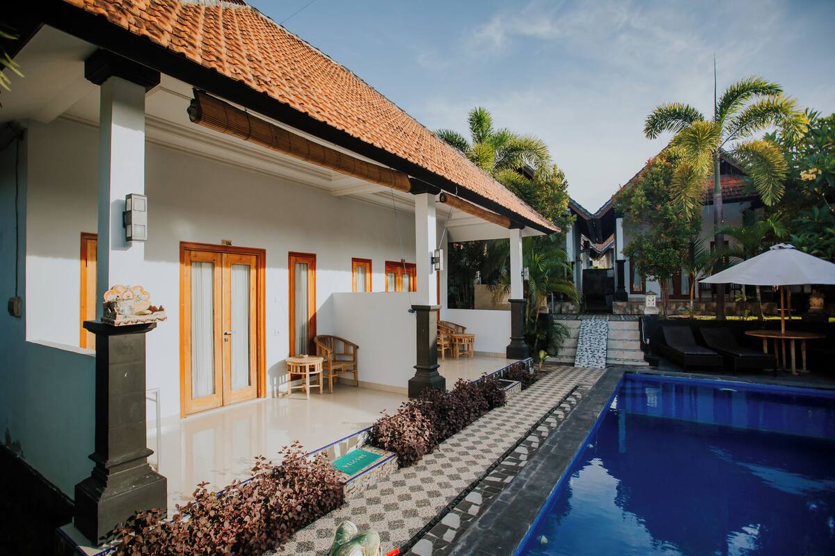 A hotel with a swimming pool, outdoor seating, and a tiled roof.