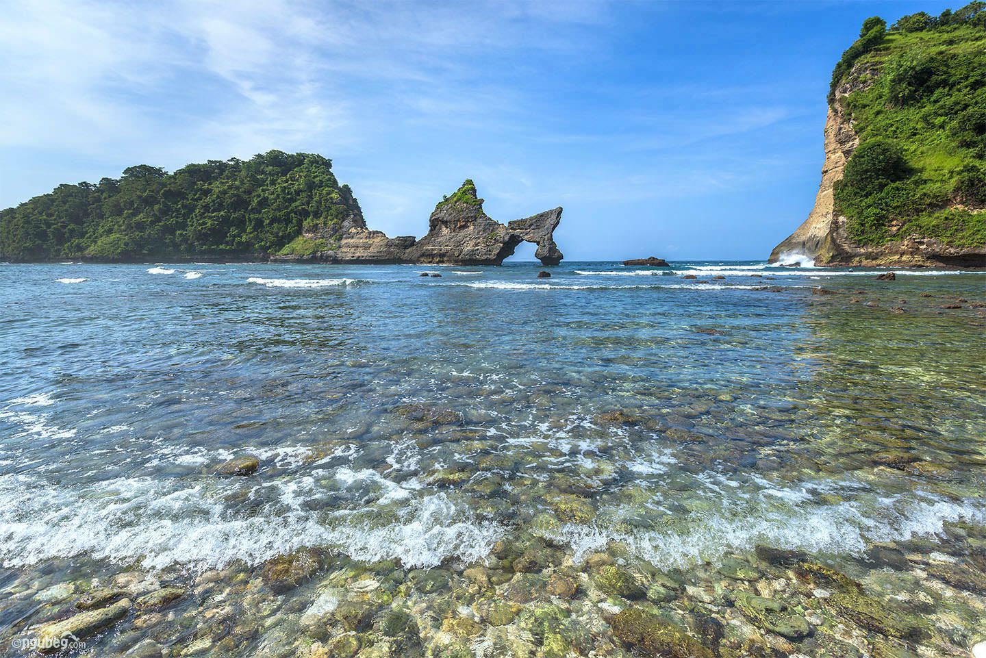 A coastal landscape with clear water, rocky formations, and lush greenery.