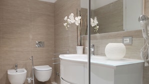 A modern bathroom with a bidet, a toilet, a large sink, and a glass shower enclosure.
