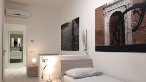 A bedroom with a bed, bedside table, lamp, and a large framed picture on the wall.