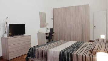 Quarto de hotel moderno com cama, escrivaninha, televisão e guarda-roupa.
