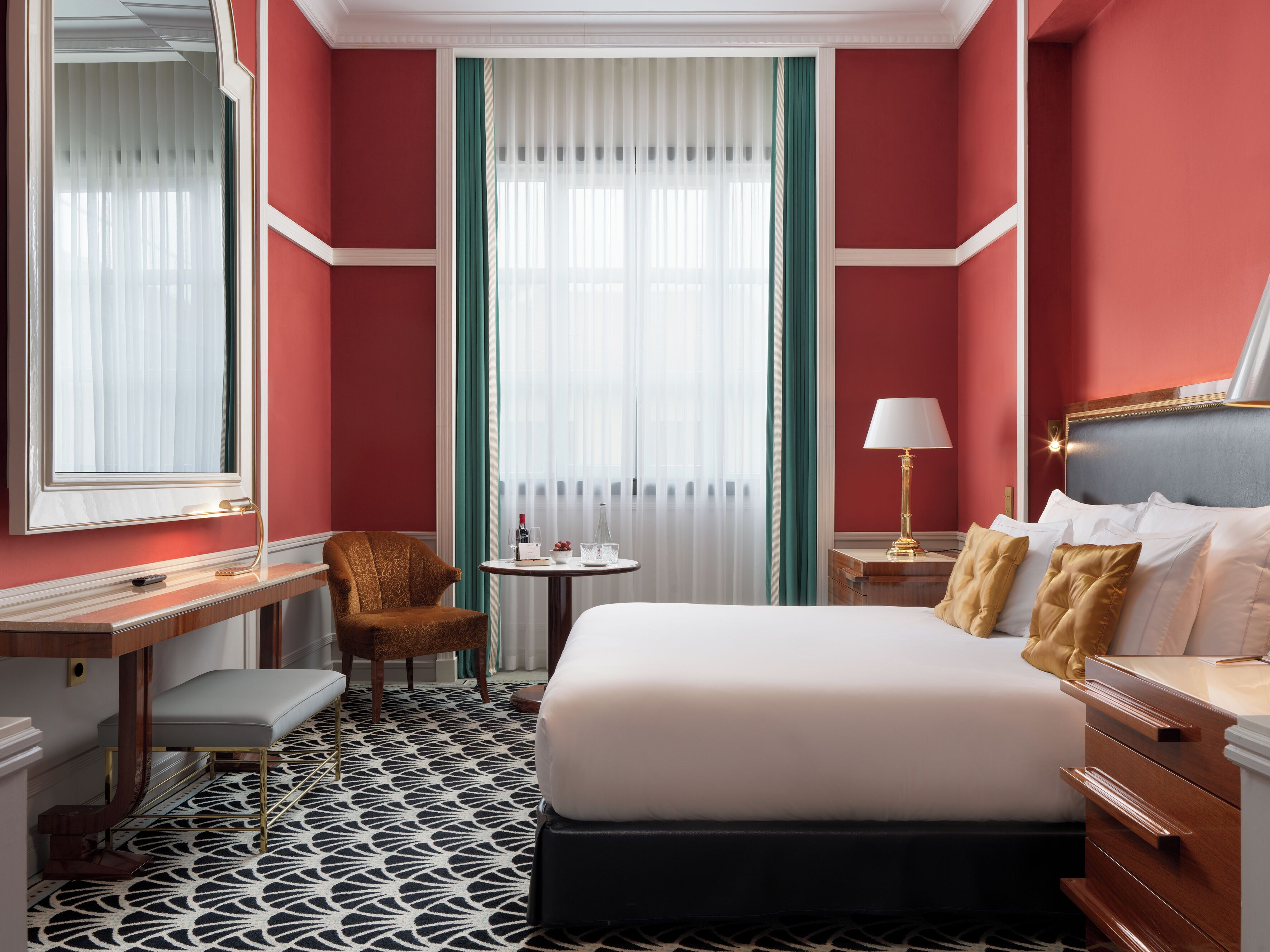 Habitación de hotel con cama, escritorio, silla, mesita y ventana con cortinas.
