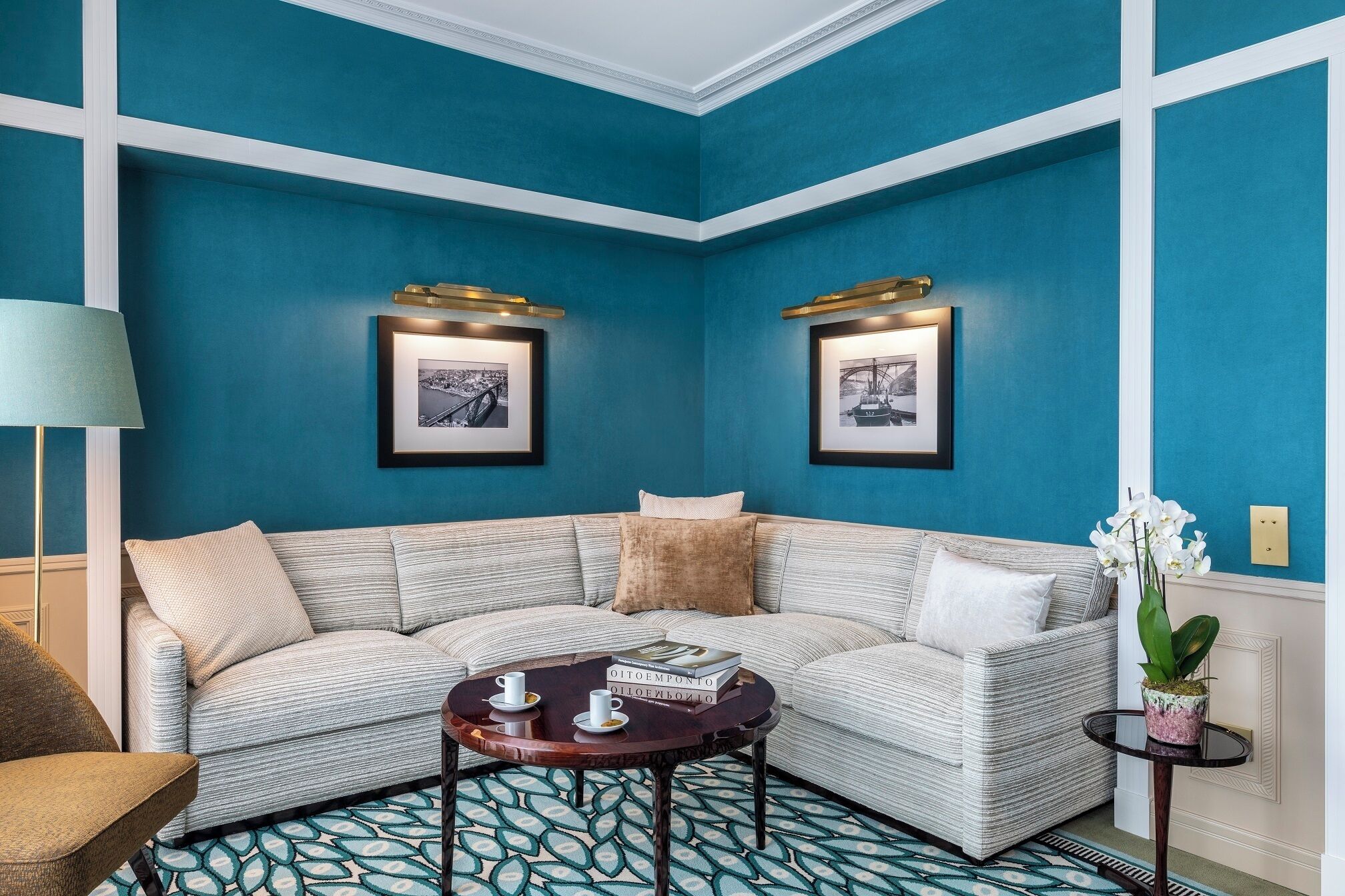 Una habitación con una pared azul, un sofá de esquina, una mesita redonda y dos cuadros enmarcados.