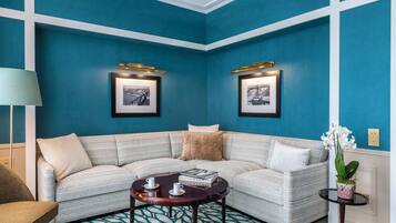 Una habitación con una pared azul, un sofá de esquina, una mesita redonda y dos cuadros enmarcados.