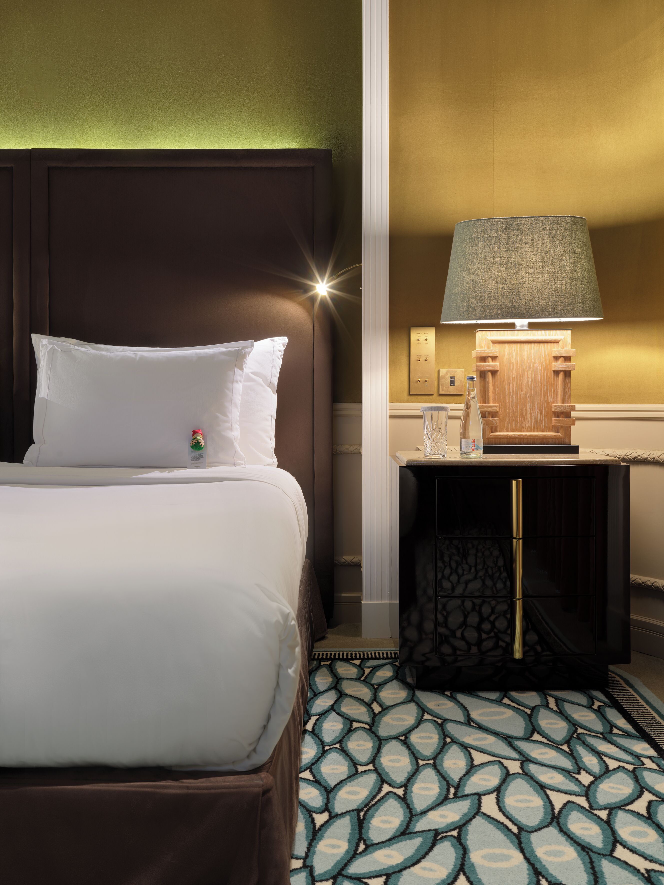 Een hotelkamer met een bed, een nachtkastje met een lamp en een kamerbreed tapijt met dessin.