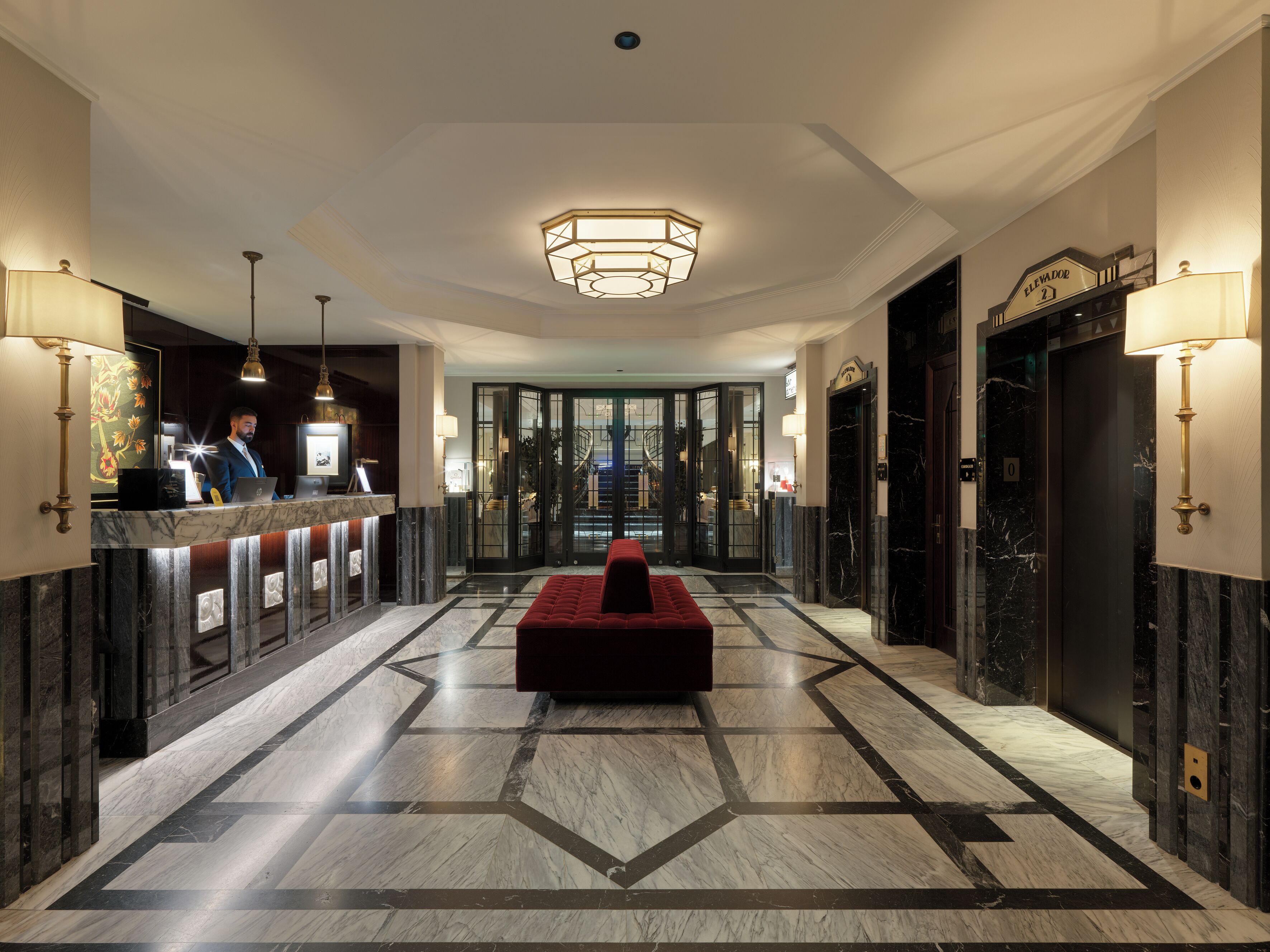 Un vestíbulo de hotel con mostrador de recepción, una zona de estar roja y un suelo con patrón geométrico.