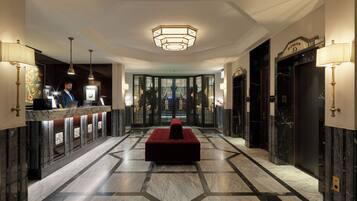 Un vestíbulo de hotel con mostrador de recepción, una zona de estar roja y un suelo con patrón geométrico.