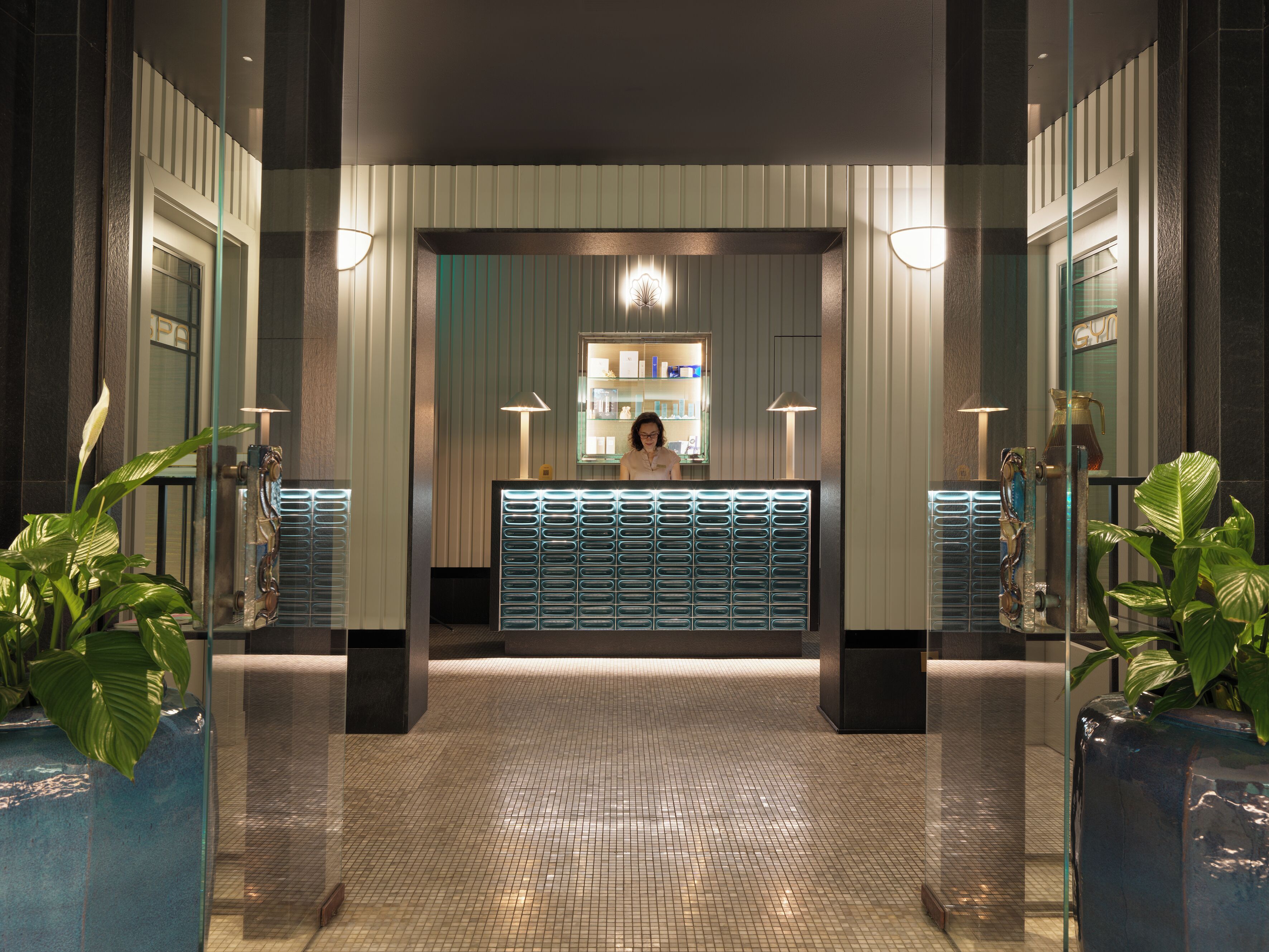 A reception area with a counter, a mirror, and a person standing behind it.