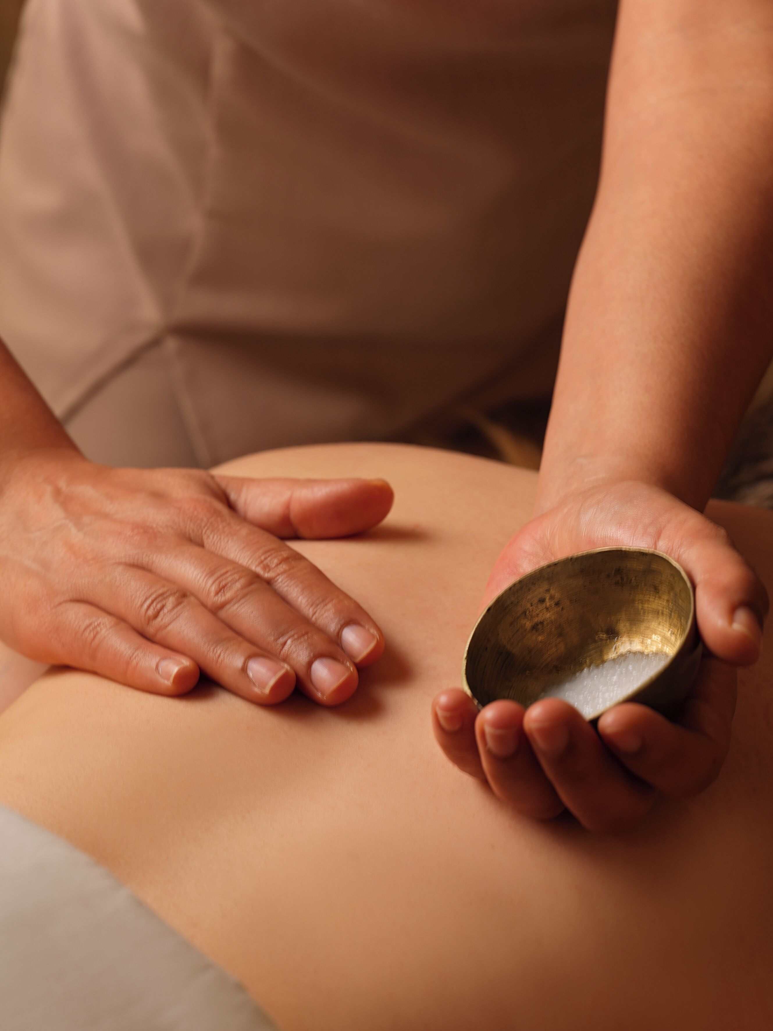 A person holding a bowl over another person's back, likely in a massage or therapeutic setting.