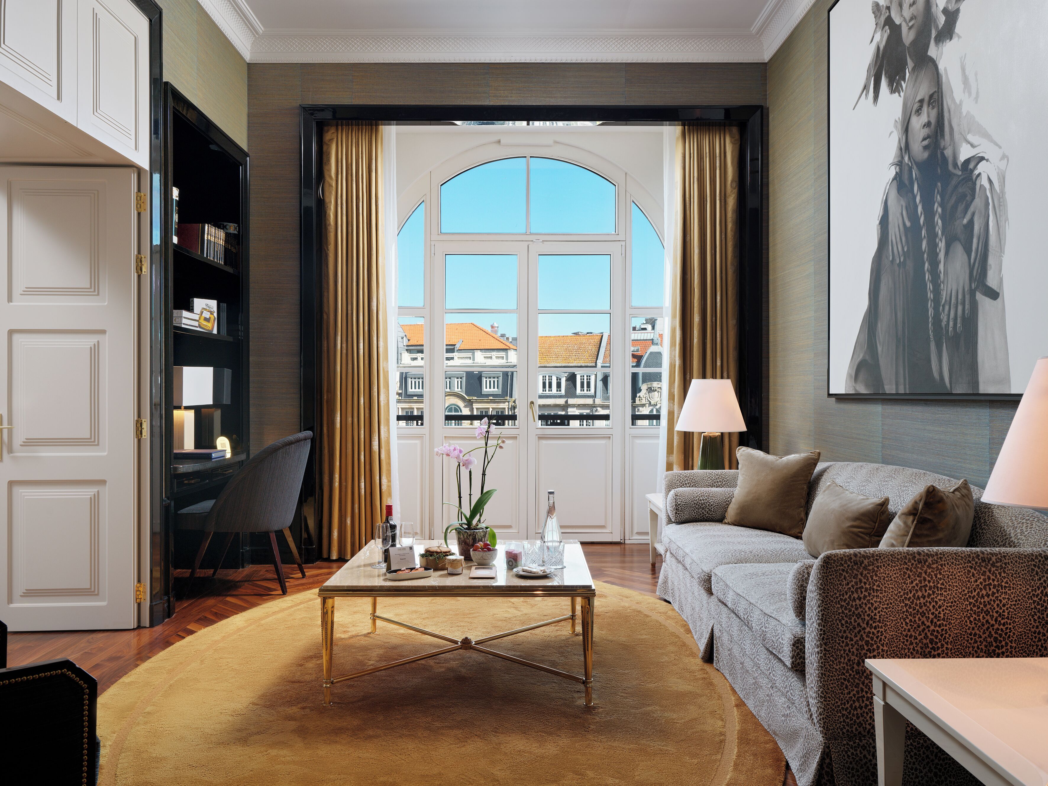 Habitación de hotel con vista a edificios, un sofá, una mesa de centro, una silla y una estantería.