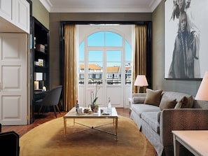 Habitación de hotel con vista a edificios, un sofá, una mesa de centro, una silla y una estantería.
