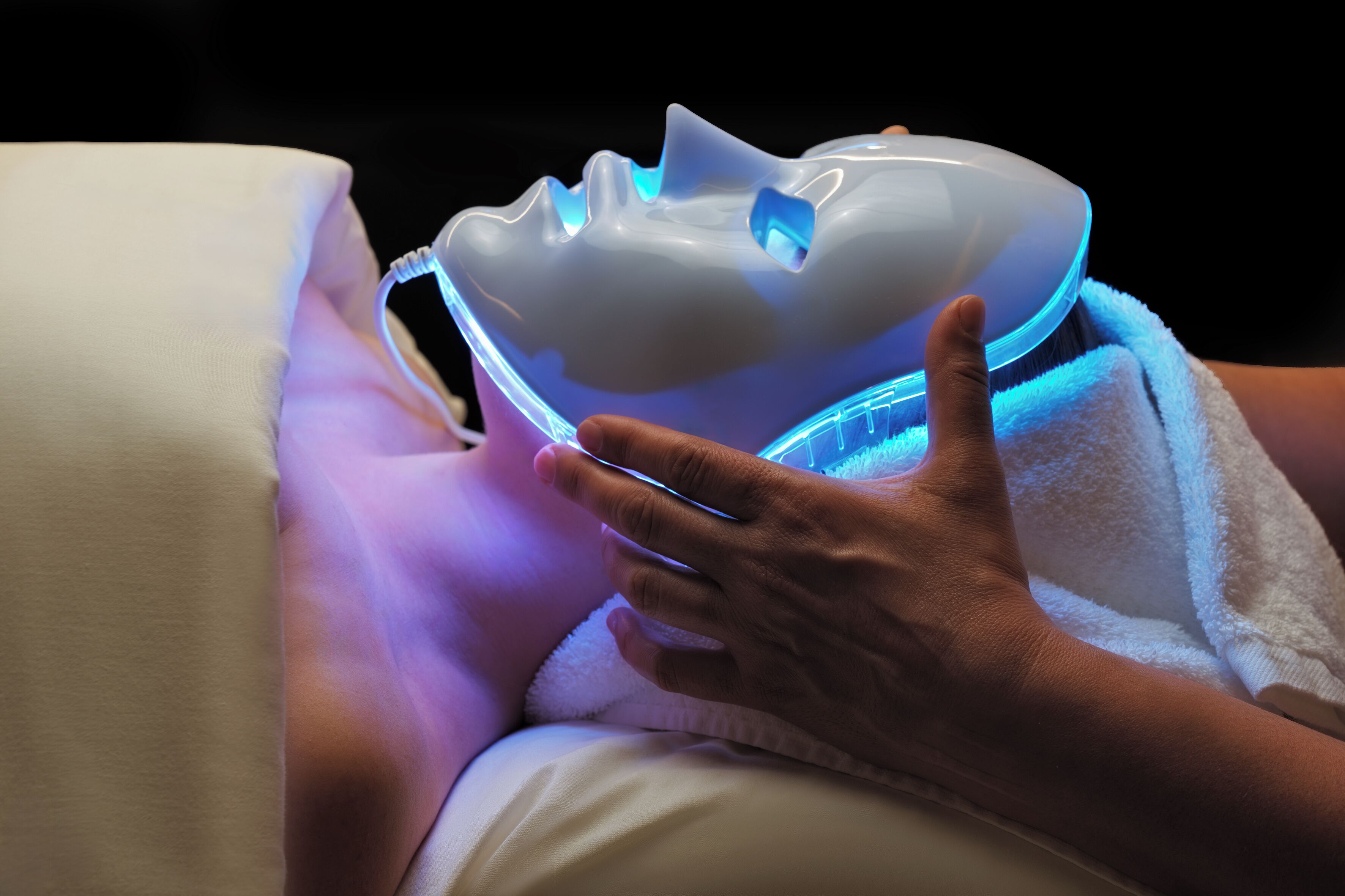 A person lying down with a white pillow and a device emitting blue light.