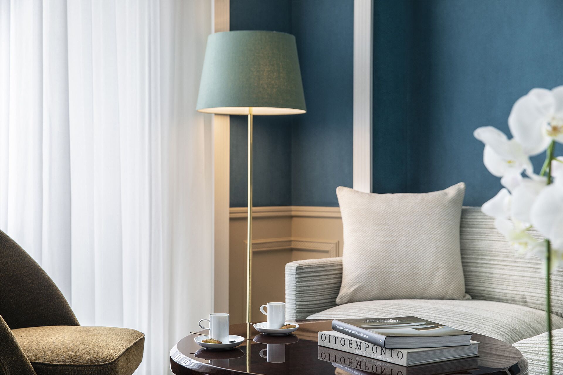 Una habitación con un sofá, una mesa de centro con libros, una lámpara y una ventana con cortinas.