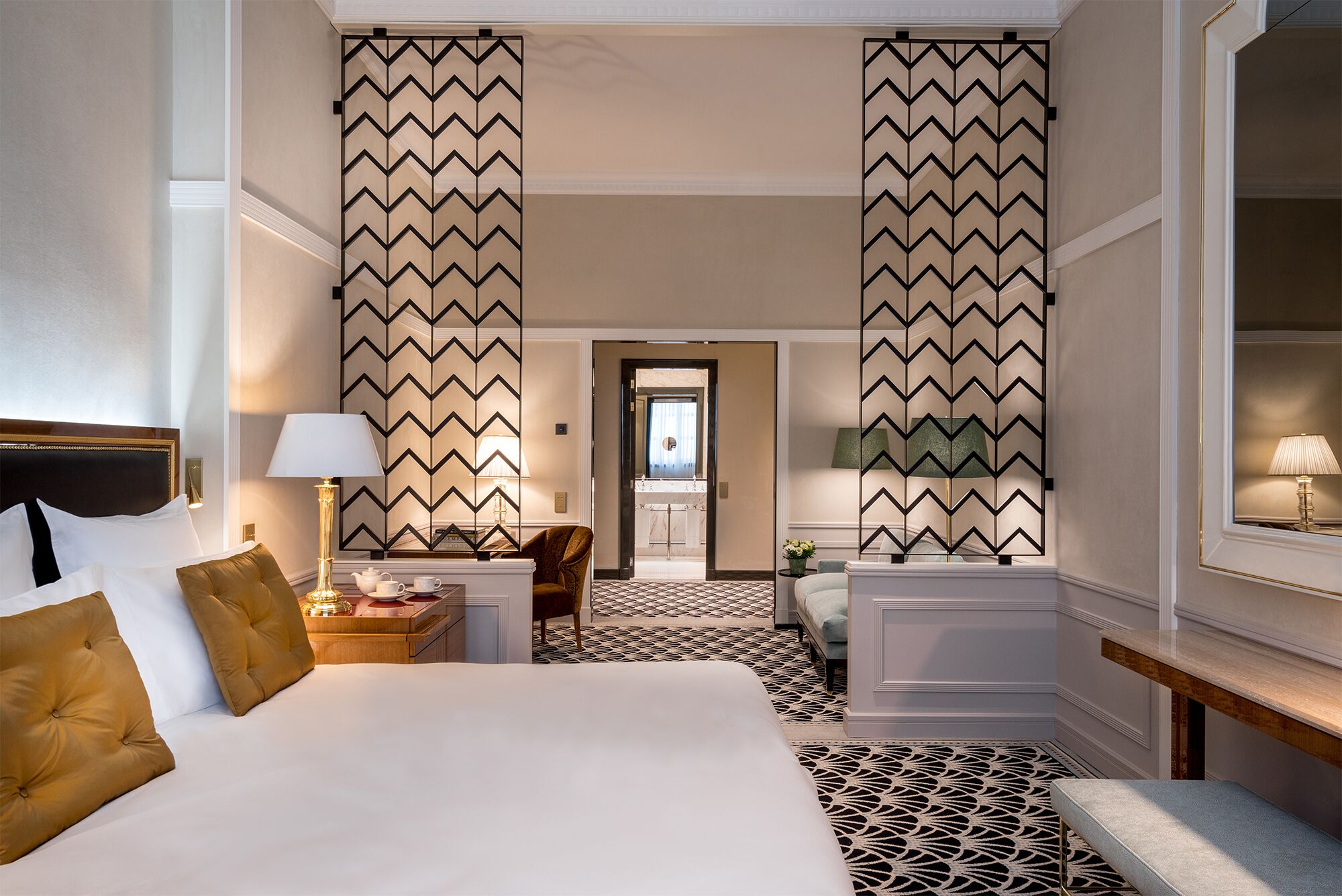 A hotel room with a bed, bedside tables, a lamp, a chair, and a view of the bathroom.