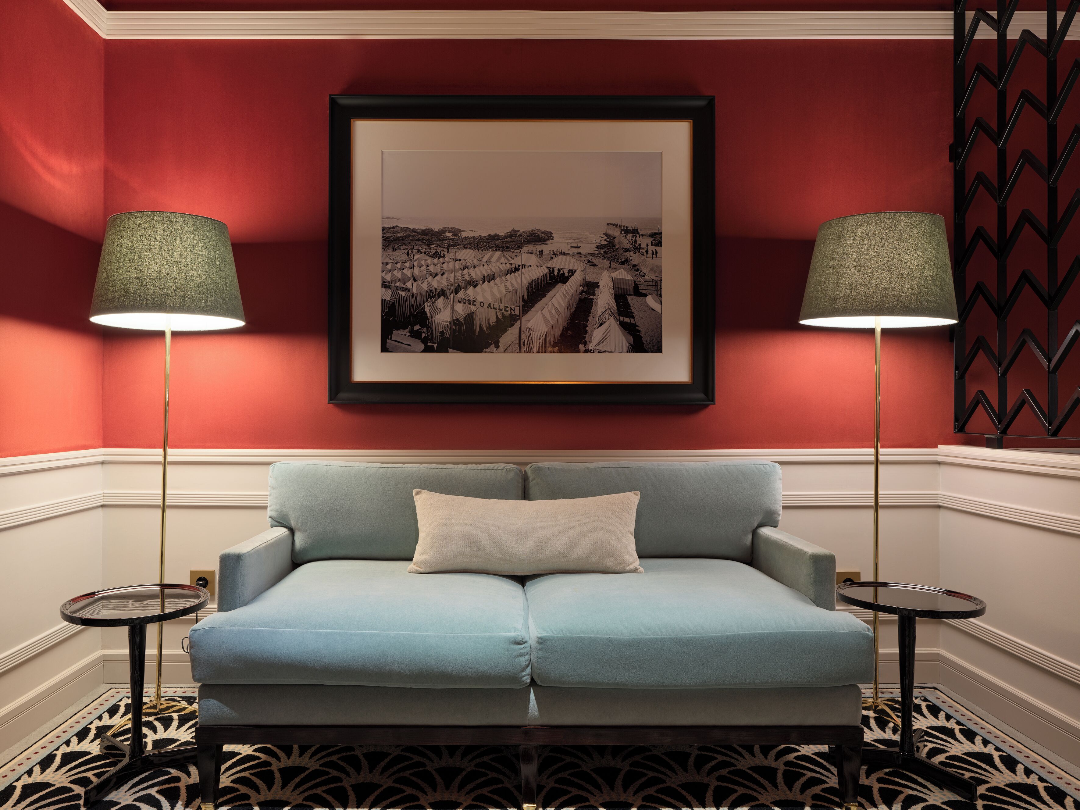 A room with a light blue sofa, two floor lamps, a framed black and white photograph on the wall, and a patterned carpet.