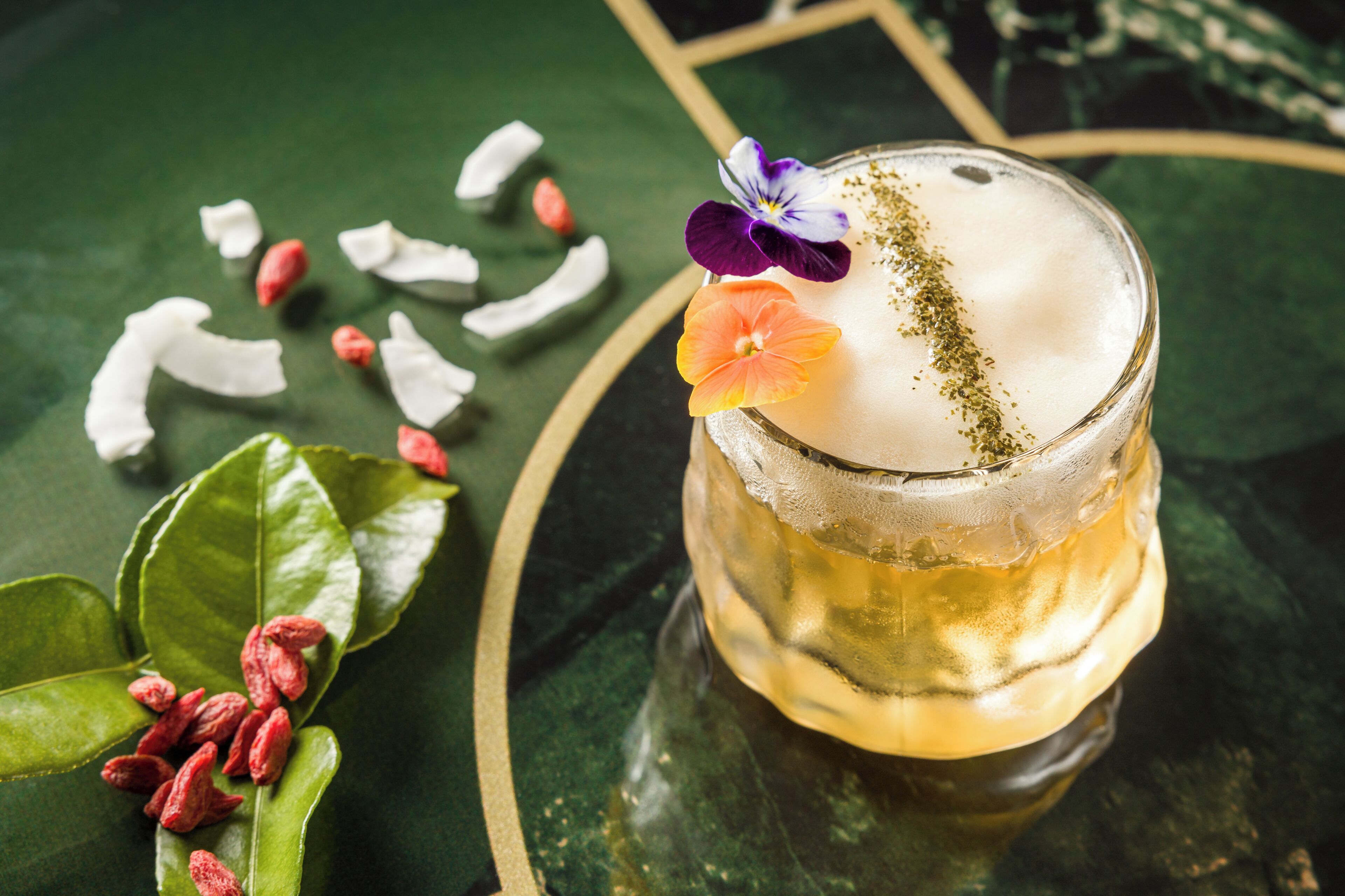 A glass of a beverage with a garnish, surrounded by green leaves and red berries.