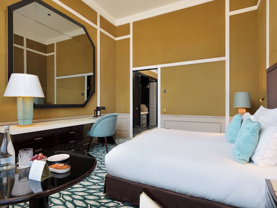 Habitación de hotel con una cama grande, un escritorio con lámpara, una silla y un espejo.